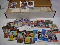 Large box filled with about 1000 baseball cards, some pulled out and displayed showing a variety of players and teams.