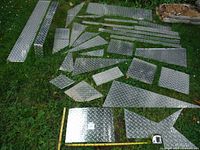 Multiple aluminum diamond plate off-cut pieces laid out on grass showing various sizes and rectangular shapes.