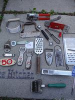 Overview of all 20 vintage kitchen tools laid out on outdoor surface including antique can opener, graters, openers, peelers and cutters.