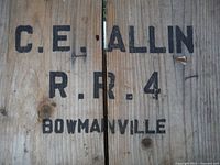 Close-up of the black stenciled text C.E. Allin R.R. 4 Bowmanville on the crate's wooden slats.