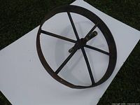 Antique metal wheelbarrow wheel lying on a white background, showing six rusted iron spokes and rim.