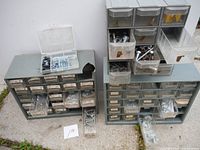 Three metal storage units with multiple small drawers containing various small hardware items such as screws, bolts, nuts, washers, and fasteners.