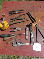 Set of antique hand tools laid out on a red surface including pliers, wrenches, pincers, screwdrivers, and an oil can.
