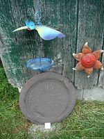 Bird feeder, metal garden sun plaque, and ceramic sun face hanging against weathered wooden surface.