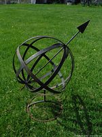 Front view of a metal armillary-style garden ornament placed on grass, showing spherical bands and arrow detail