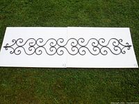 Full view of large metal scrollwork decorative piece on grass, showing length and shape