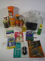 Full overview of the lot with fish bowl, multiple bottles of fish food and treatments, feeding accessories and smaller boxed items.