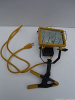 Yellow halogen work light with attached yellow power cord and clamp base on white surface.