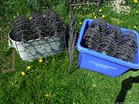 Lot of stacked black metal garden fence panels with green glass inserts, shown in two large bins on grass.