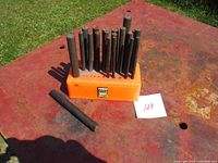 Set of metal center punches arranged in an orange plastic stand on a rusty metal surface.