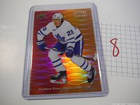 Hockey card showing Matthew Knies in Toronto Maple Leafs jersey number 23 on red/orange holographic Allure Color Flow background.