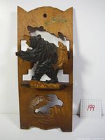 Front view of the wooden letter rack showing a 3D carved bear atop a platform and a carved fish below. The wood has a natural finish with decorative carved edges and a signature near the top.