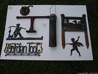 Top-down view of seven metal garden items including stakes, signs, and a hanging basket holder arranged on a white surface.