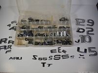 Assorted chrome automotive letter emblems organized in plastic case compartments and some outside the case