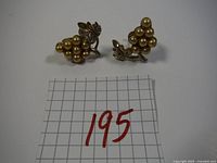 Pair of vintage clip-on earrings with cream faux pearl clusters and gold-tone metal leaf accents with rhinestones shown on a grid for scale.