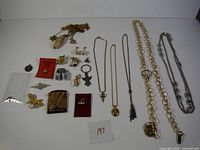Top-down photo showing assorted vintage jewelry laid out on white background including necklaces, pins, brooches and charms.