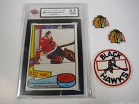 Photo of 1980-81 Tony Esposito hockey card graded 8.5 near mint plus in protective case alongside three Chicago Blackhawks embroidered patches.