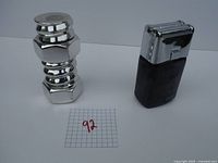 Chrome nut and bolt shaped bottle and vintage Avon electric razor against a white background with a grid paper labeled '92'