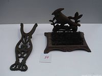 View of the vintage cast iron boot jack alongside the cast iron boot brush with bird handle, both shown on a white background with a paper label 54.