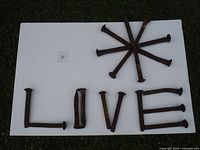 18 old railroad spikes arranged to spell 'LOVE' and some in a star shape, showing overall quantity and condition