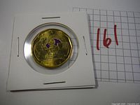 Photo of the UNC Oscar Peterson Loonie showing full coin in holder with part of grid paper with handwritten 161.