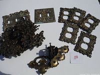 Photo displaying multiple ornate vintage metal switch plates and decorative metal drawer pulls and handles on a white background.