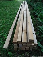 Stack of multiple pressure treated lumber pieces laid on grass, showing length and condition