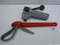 Two tools: an orange handled Rigid strap wrench with fabric strap and a metallic Greenlee flexible conduit cutter with measurement scale and cutting wheel.