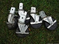 Five scaffold caster wheels with metal mounting plates and brakes arranged on grass.