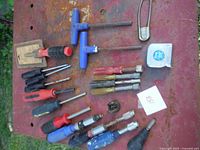 Overview of screwdrivers, nut drivers, T-handle tools, and tape measure laid out on a red surface.