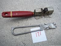 Sharpener with red wooden handle and cylindrical metal dual sharpening heads photographed on concrete surface with paper marked '171'