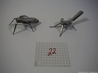 Two handmade bug sculptures made from metal forks shown on a plain background near measurement grid.