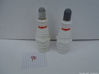 Two vintage Avon bottles shaped like Champion spark plugs, one with gray cap and one with black cap, sitting on white background with number 90