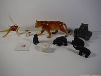 Photo showing the full assortment of animal figurines including the large brown ceramic lion, glass fish, small ceramic dog, white rabbit, and several black matte figurines resembling various animals.