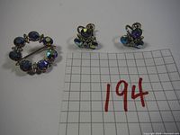Photo showing the full jewelry set with circular brooch and two clip-on earrings alongside a grid background marked 194