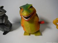 Front view of the yellow-green wind-up dinosaur with a red wind-up key.