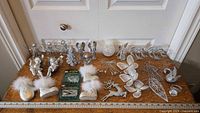 Wide photo of entire assortment of white and silver Christmas ornaments displayed on wooden table.