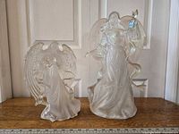 Two acrylic angels placed side by side on a wooden surface in front of a white door, showing front view with ruler for size reference.