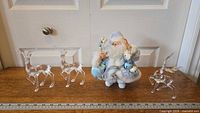 Santa Claus figurine and three acrylic reindeer on a wooden surface with door in background