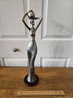 Front view of the African tribal female sculpture with ruler for scale on wood surface in front of white paneled door.