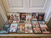 Photo of 14 assorted DVD movie cases laid out on floor in two rows against wall, titles visible