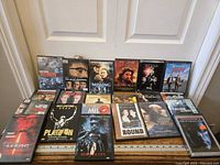 Eleven assorted DVDs arranged in two rows leaning against a door. Titles include Ronin, The Good Shepherd, Gladiator, Predator, Children of Men, Platoon, Mission to Mars, Bound, Moonlight Mile, The Departed.