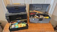Four toolboxes on a wooden surface with assorted hand tools inside