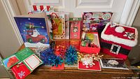 Christmas gift wrap and accessories arranged on a table including gift bags, tags, tinsel garlands, and a decorative storage box.