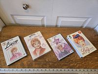 Four different I Love Lucy DVD box sets arranged on a wooden surface showing front covers, each featuring Lucille Ball as the main subject in various photos and titles.