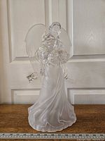 Front view of the 9 by 18 inch acrylic praying angel tree topper standing on a wooden surface against a white paneled door.