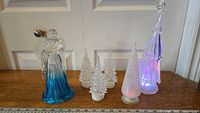 Photo of all items on wooden surface showing angel and three acrylic Christmas trees with light-up features.