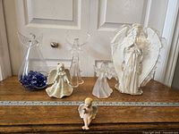 Photo showing all six angel figurines placed on a wooden surface next to a ruler for size reference, displaying variety in size, material and color.