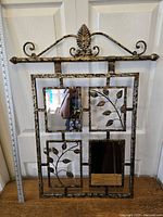 Front view of metal decorative wall mirror with four portion design showing branched leaf metalwork and beveled glass mirror sections.