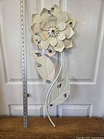 Full view of metal flower wall art next to measuring ruler showing size approx 11 inches wide by 32 inches tall